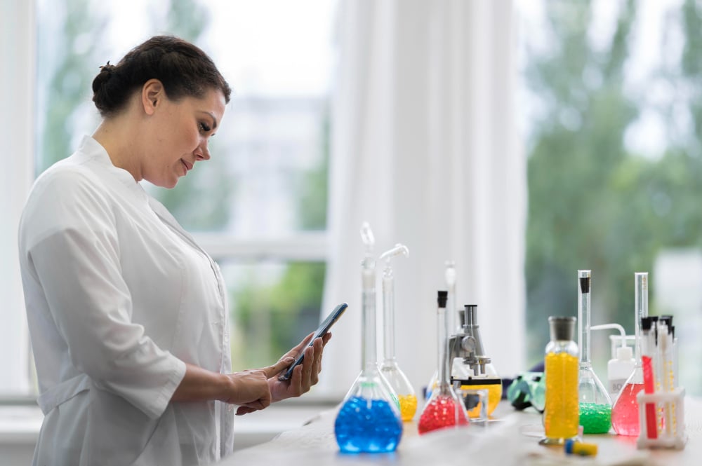 Scientist in white coat examining tablet by laboratory equipment